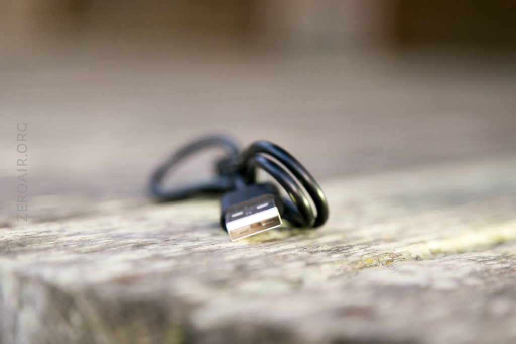 A black USB-A cable with a coiled cord lies on a wooden surface, with the USB connector in focus and the background blurred.