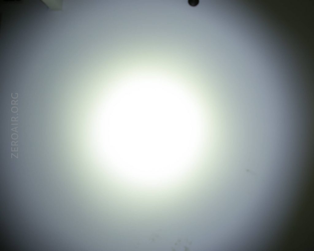 A bright white circular light is centered on a gray surface, creating a gradient effect. The text ZEROAIR.ORG is faintly visible along the left side. Some small marks are on the lower part of the surface.