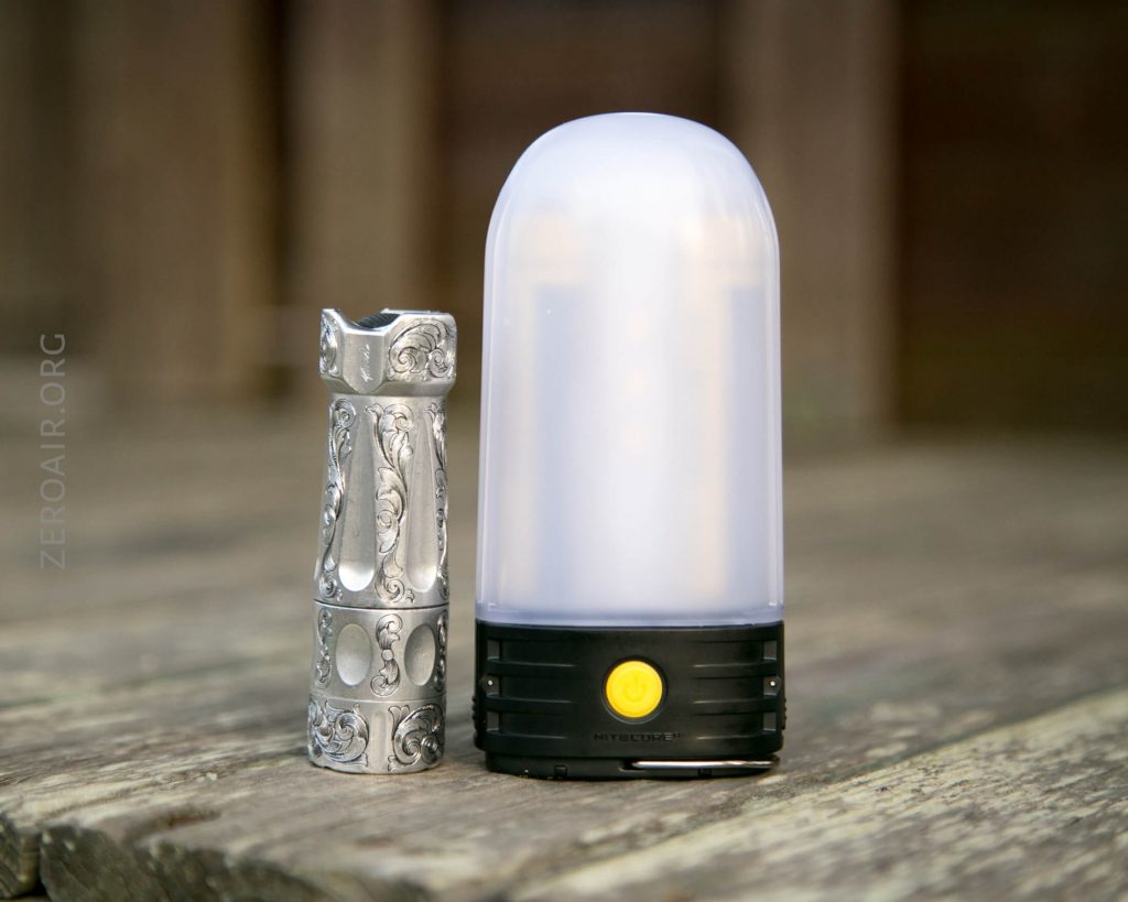 A decorative silver flashlight stands next to a black and white lantern with a yellow power button, both placed on a wooden surface.