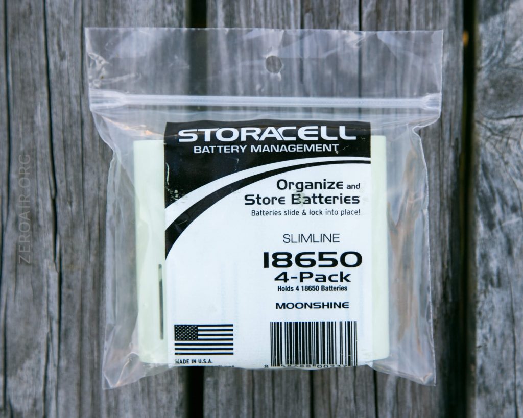 A clear plastic bag containing a Storacell Battery Management 18650 4-pack, designed to organize and store batteries. The packaging displays the product information and an American flag symbol. The bag is on a wooden surface.