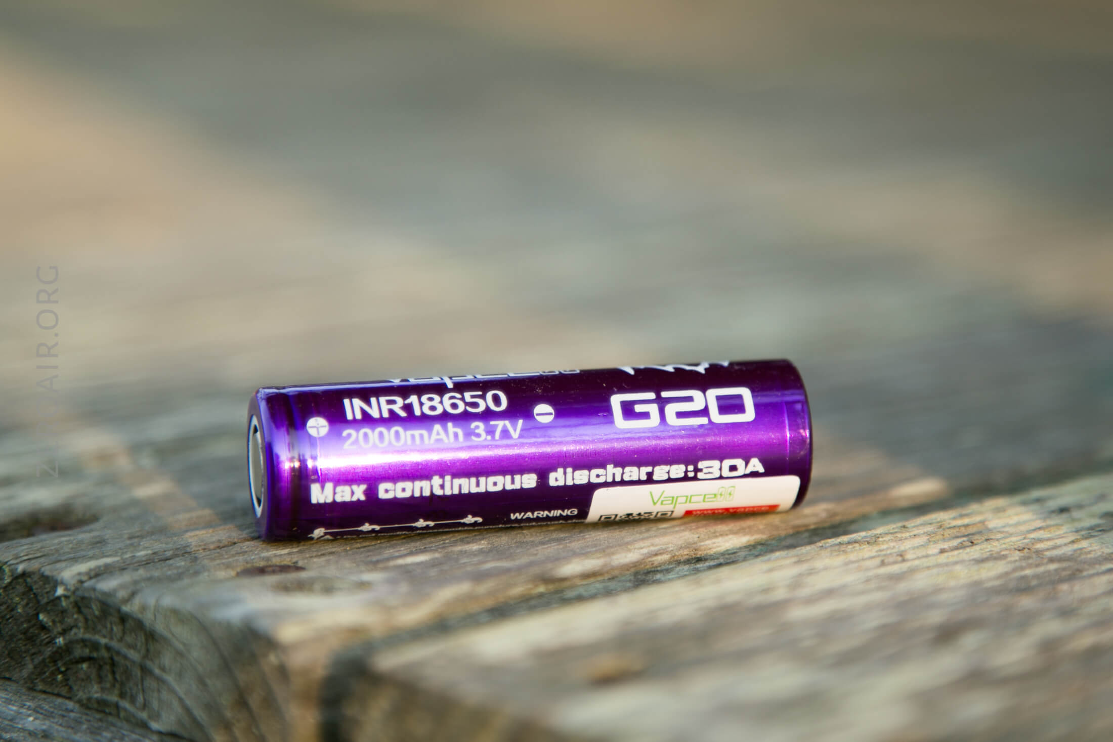 A purple INR18650 G20 battery with 2000mAh capacity and 3.7V rating lies on a wooden surface. The label notes a max continuous discharge of 30A.