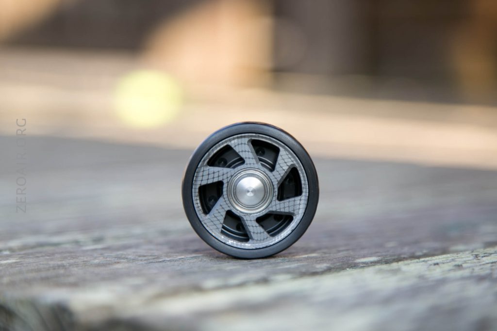 A close-up of a single gray and black wheel with a metallic center, resting upright on a wooden surface with a blurred background.