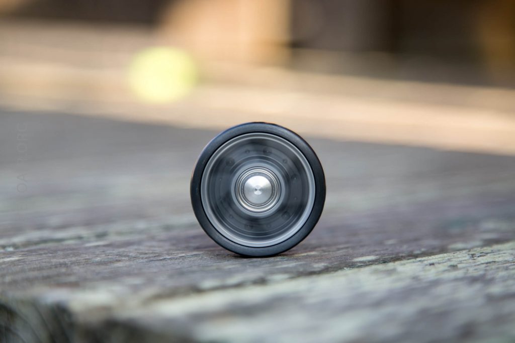 A close-up of a black and silver yo-yo standing upright on a weathered wooden surface with a blurred background.