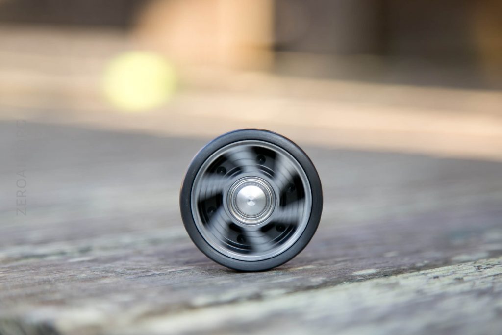 A black yo-yo spinning on a weathered wooden surface, with the background blurred and out of focus.