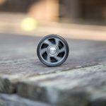 A black yo-yo is spinning in motion on a weathered wooden surface, slightly out of focus in the foreground, with a blurry background.