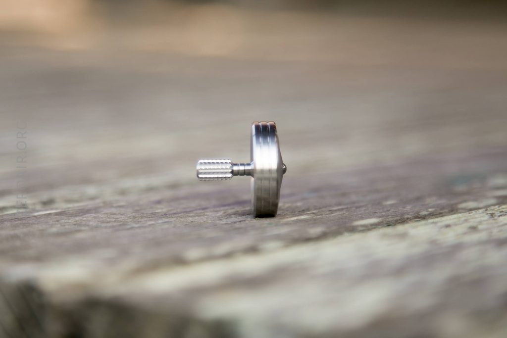 A small metal spinning top standing upright on a wooden surface, with the background blurred.
