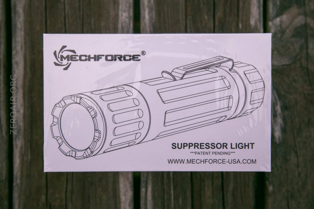 A white box labeled MechForce Suppressor Light with a black line drawing of a tactical flashlight. The website www.mechforce-usa.com is printed on the front. The box is on a wooden surface.
