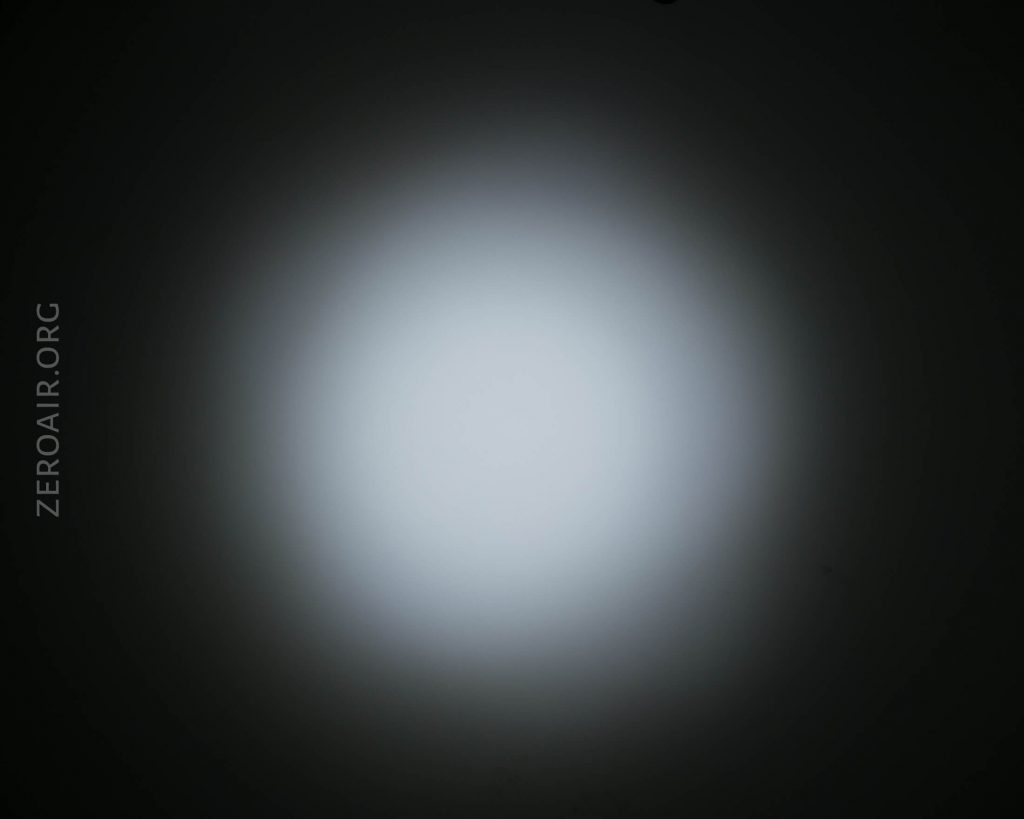 A circular beam of white light with a bright center and darker edges is projected onto a flat surface. The text ZEROAIR.ORG is visible vertically on the left side.