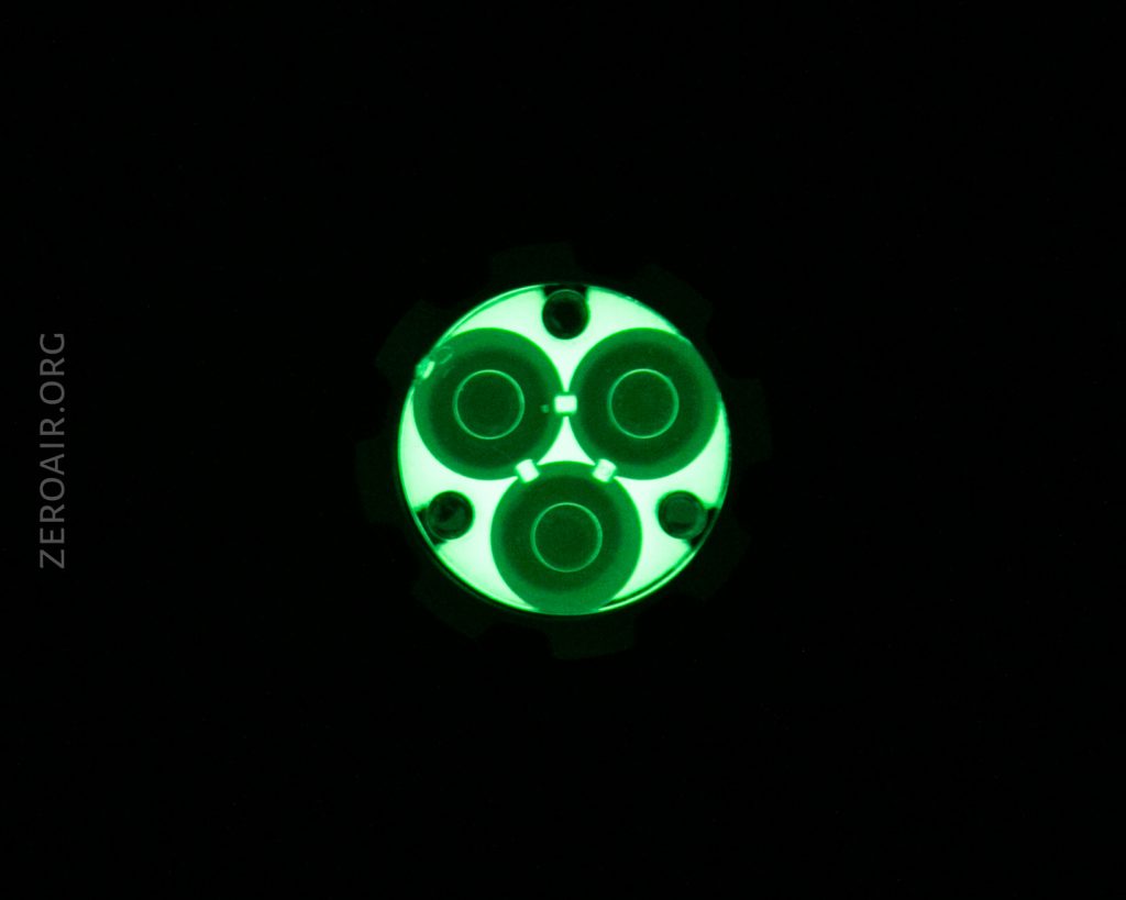 A round object with three circular shapes inside glows green in the dark, against a black background. The text ZEROAIR.ORG appears vertically on the left side.