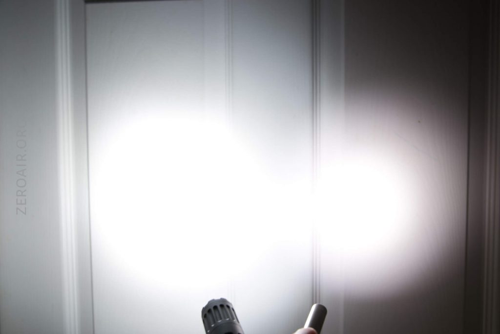 Two bright flashlight beams are projected onto a white door, creating overlapping, illuminated circles on the surface. The flashlights themselves are partially visible at the bottom of the image.