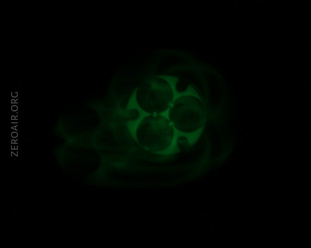 A dark image shows a faint, green, glowing pattern resembling overlapping circles and swirls. The background is black, and “ZEROAIR.ORG” appears vertically on the left side of the image.
