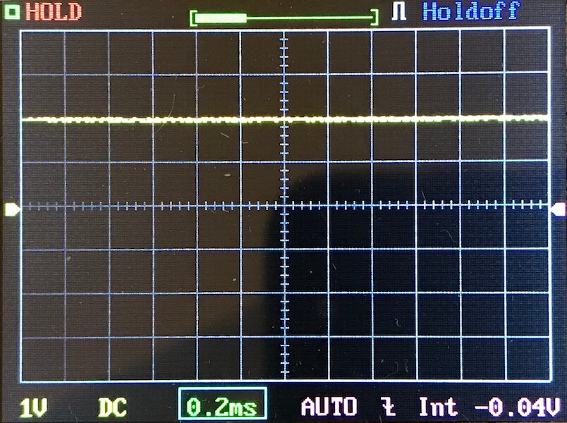 An oscilloscope display shows a flat, horizontal yellow line near the center of the screen, indicating no significant signal variation. The time base is set to 0.2 ms per division and the voltage is set to 1V per division.