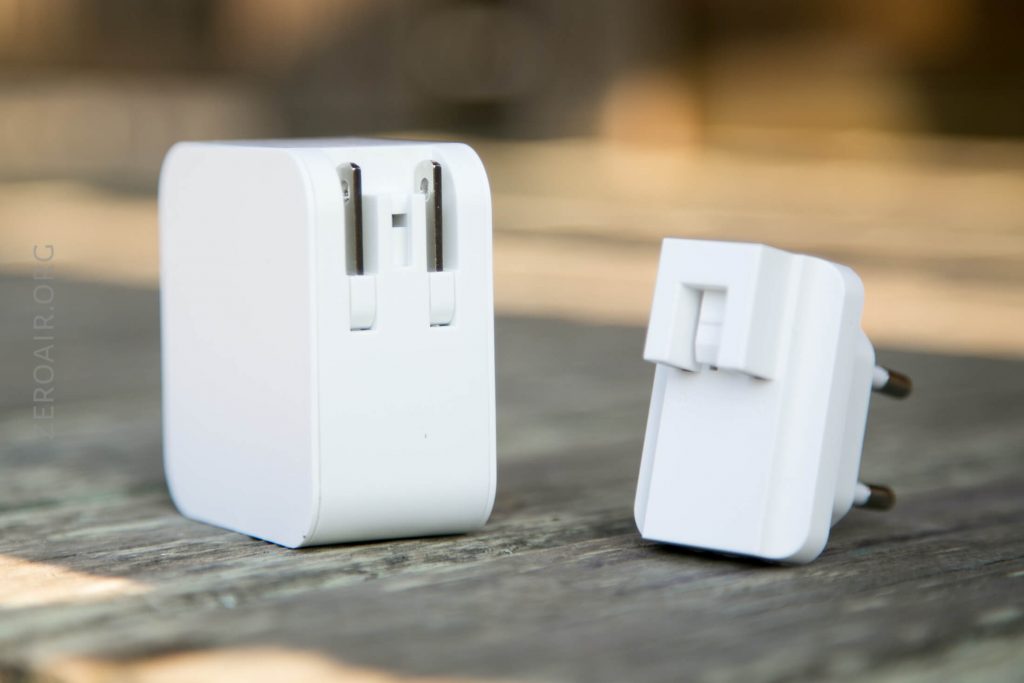 Two white electrical adapters are placed on a wooden surface. One shows foldable prongs retracted, and the other displays plug pins and a slot on its back. Both adapters appear compact and minimalist in design.