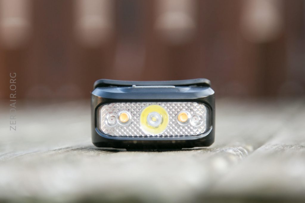 A close-up view of a rectangular LED bike light with four bulbs and a reflective surface, resting on a wooden surface with a blurred brown background.