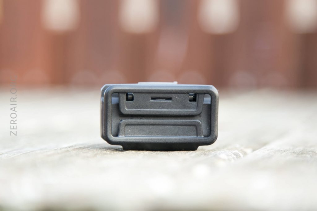 A close-up, front view of a rectangular black electronic device or component, placed on a wooden surface with a blurred background. The device features a slot and two small rectangular openings.