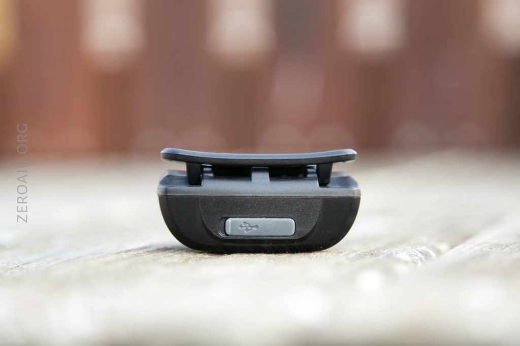 A close-up view of a small black electronic device placed on a wooden surface, with a USB symbol visible on a button at the front. The background is blurred.