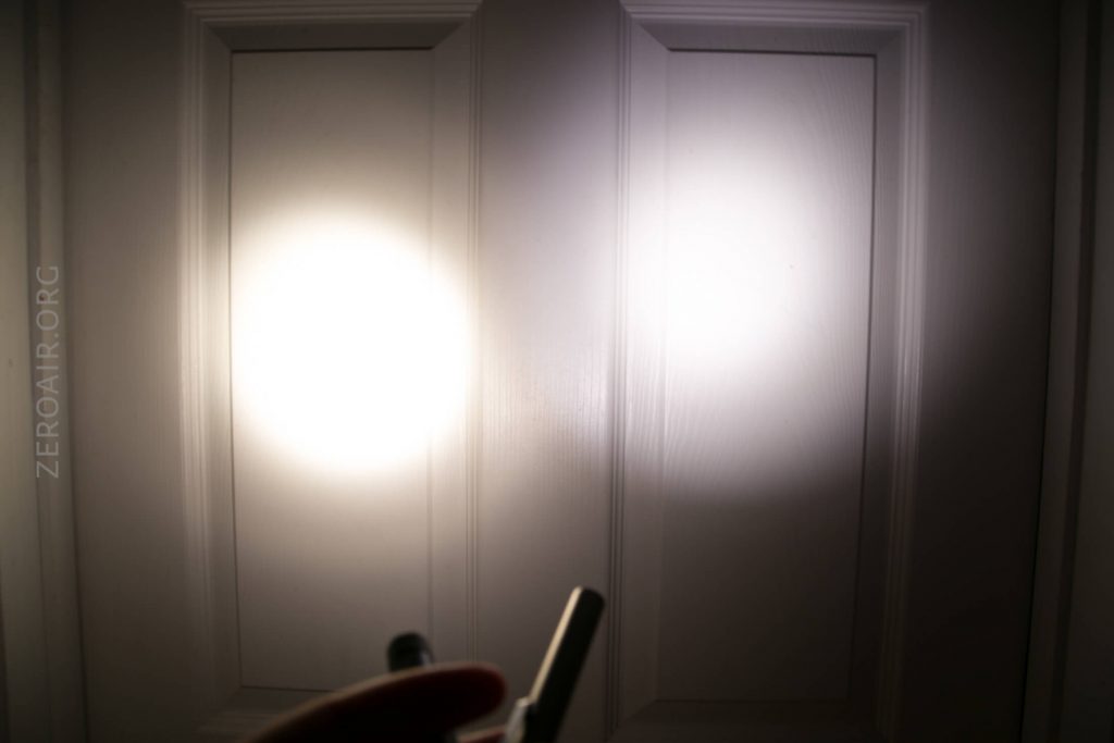 A flashlight beam is projected onto a white paneled door in a dark room. Two distinct circles of light are visible, and part of a hand holding an object is at the bottom of the image.