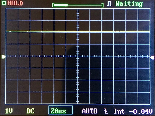 A digital oscilloscope screen displays a mostly flat yellow trace near the top, with grid lines, measurement settings at the bottom, and indicators reading “HOLD” and “Waiting” at the top.