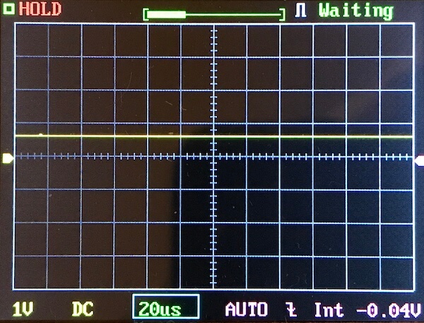 Oscilloscope screen displays a flat yellow waveform along the zero voltage axis. The display shows HOLD and Waiting status, with settings of 1V/div, 20 µs/div, DC, and a measured value of -0.04V.