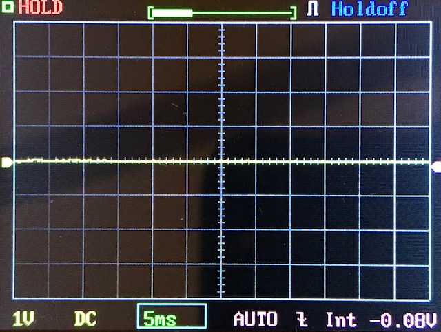 An oscilloscope screen displays a flat horizontal line at the center, with grid lines and various settings visible, including a time base of 5 ms and a voltage scale of 1V. Status indicators are shown at the top.