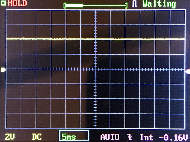 A digital oscilloscope screen displays a mostly flat yellow waveform with minor noise. Key indicators show 2V per division, 5ms time base, and a -0.16V baseline. The display reads “Waiting” and “HOLD.”