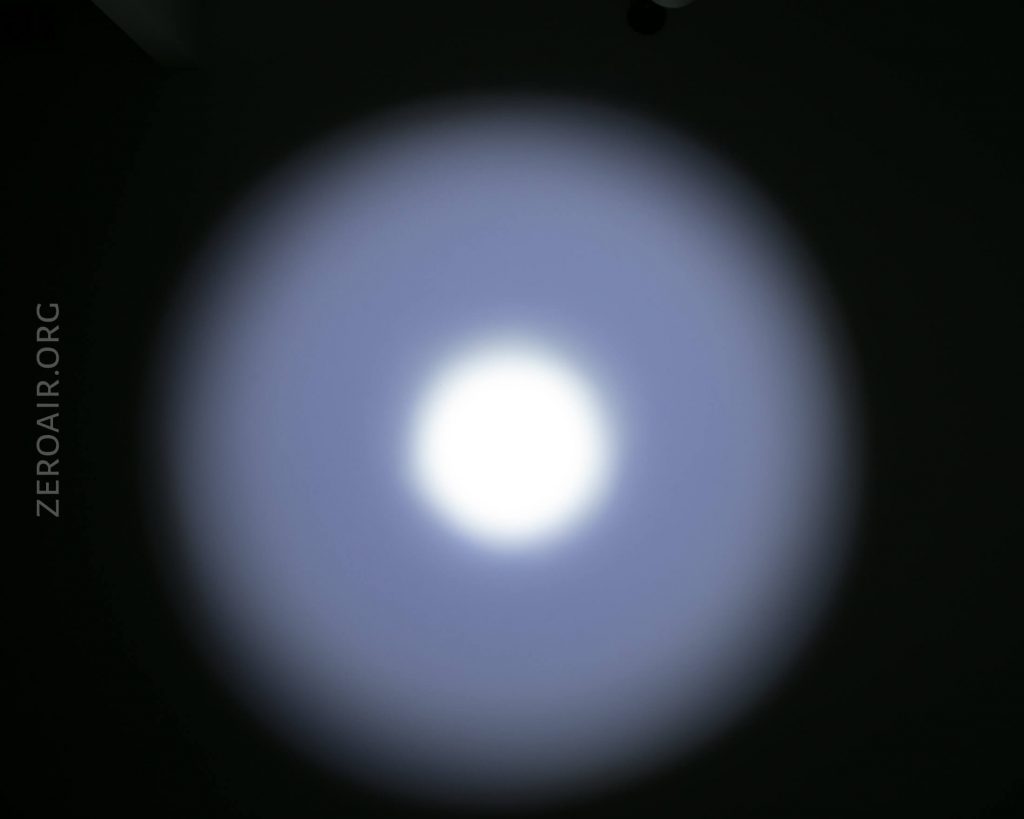 A circular white light beam with a bright center and a soft blue outer edge shines on a dark background. The watermark ZEROAIR.ORG appears vertically on the left side of the image.