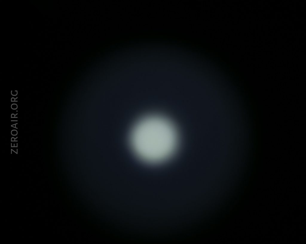 A circular, white light source is centered against a dark background with a faint blue halo around it. The text ZEROAIR.ORG appears vertically on the left side.