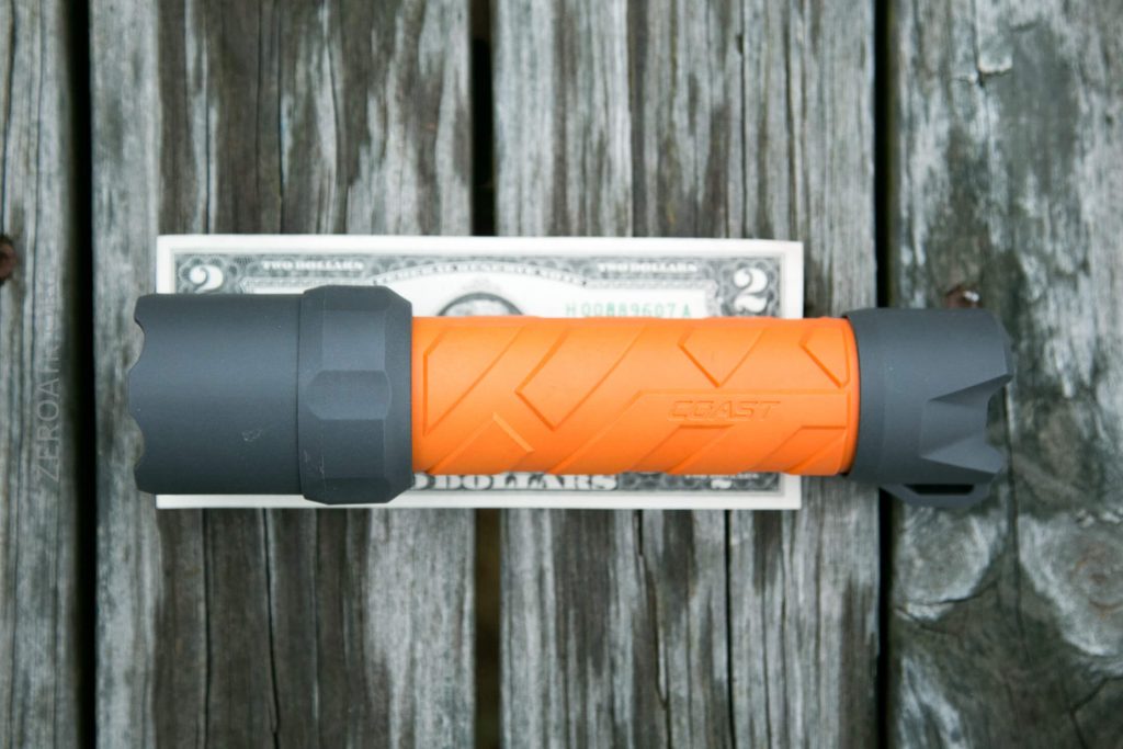 An orange and gray flashlight is placed horizontally on top of a two-dollar bill, both resting on a weathered wooden surface.