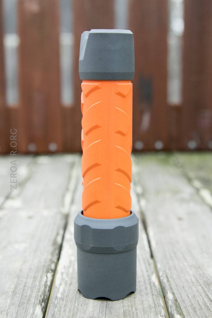 An orange and gray cylindrical object with a textured, tire-like pattern stands upright on a wooden surface outdoors.