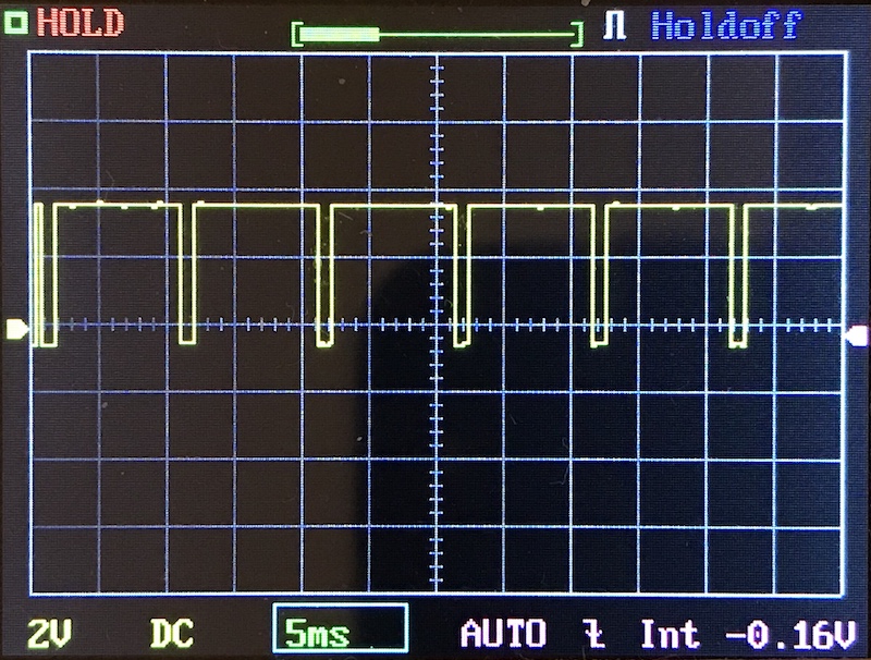 Oscilloscope display showing a yellow square wave signal with irregular pulse widths. The horizontal scale is 5 ms per division and the vertical scale is 2 V per division. Various settings are visible on the screen.