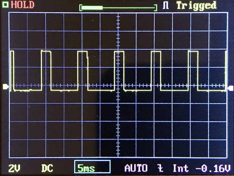 Digital oscilloscope screen displaying a square wave signal with consistent high and low pulses. The time base is set to 5 milliseconds per division, and the vertical sensitivity is 2 volts per division.