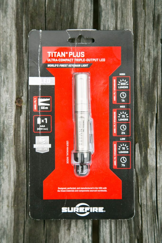 A SureFire Titan Plus ultra-compact triple-output LED flashlight in its original black and red packaging, displaying product features, specifications, and branding.