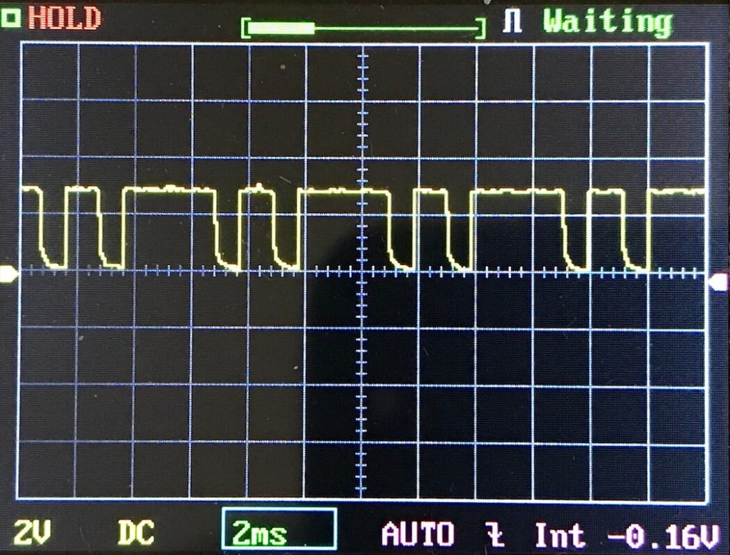 Oscilloscope screen displaying a digital square wave signal with irregular pulse widths, 2V per division vertically and 2ms per division horizontally, with the status Waiting shown at the top.