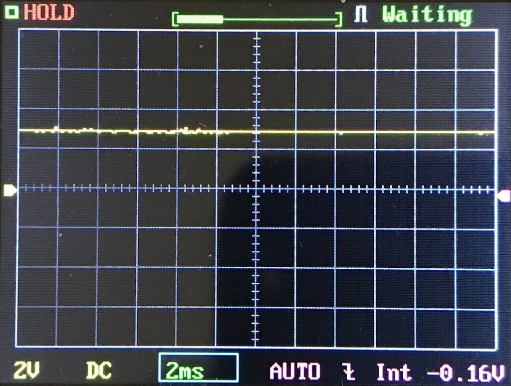 An oscilloscope screen shows a mostly flat yellow waveform near the center. The status at the top indicates HOLD and Waiting. The bottom shows settings: 2V, DC, 2ms, AUTO, and -0.16V.