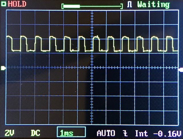 Oscilloscope screen displaying a square wave signal with regular intervals. The display shows horizontal and vertical grid lines, measurement settings, and the word “Waiting” at the top right.