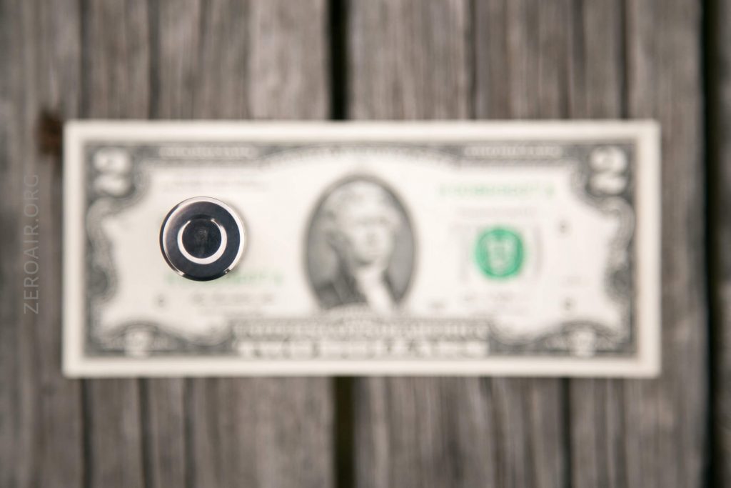 A close-up view of a flashlight’s lens pointed at the camera, with a U.S. two-dollar bill placed on a wooden surface in the blurred background.