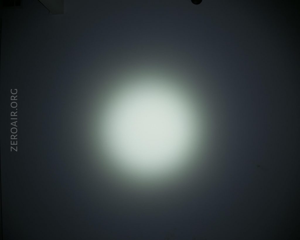 A bright, circular beam of white light is projected onto a dark wall. The words ZEROAIR.ORG are vertically printed on the left side of the image.