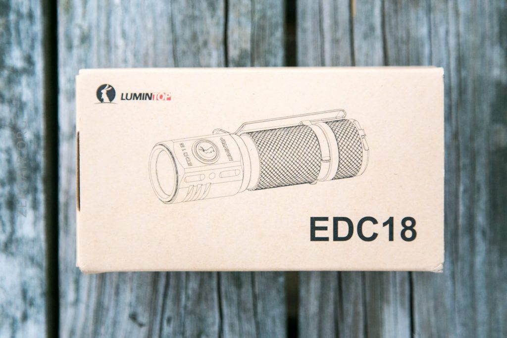 A cardboard box with a line drawing of a flashlight, the logo “LUMINTOP,” and text “EDC18” printed on it, is pictured on a wooden surface.