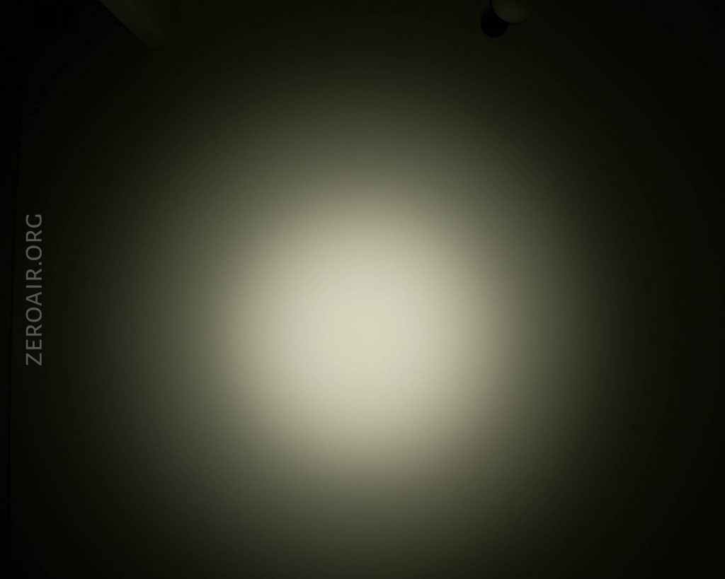 A circular beam of light is projected onto a plain, dark surface, creating a gradient from bright white in the center to dark at the edges. The text ZEROAIR.ORG appears vertically on the left side.