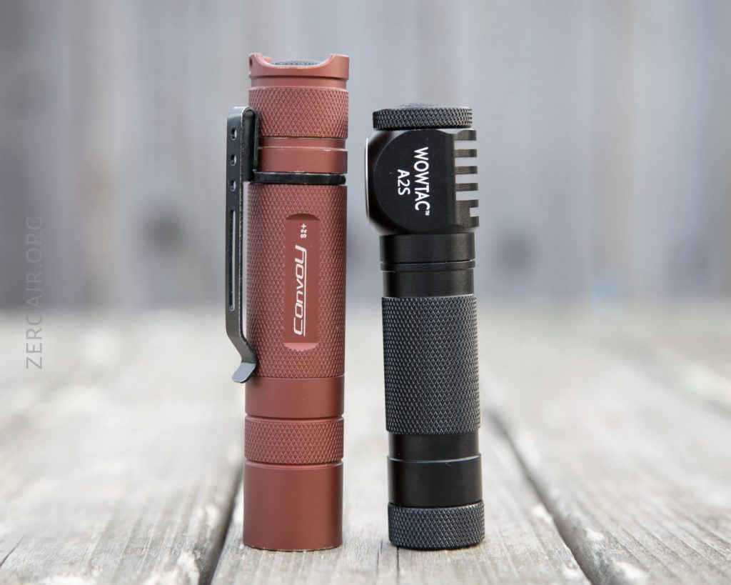 Two flashlights standing upright on a wooden surface; the left one is red with Convoy branding and a clip, and the right one is black with WOWTAC A25 branding and a ribbed head.