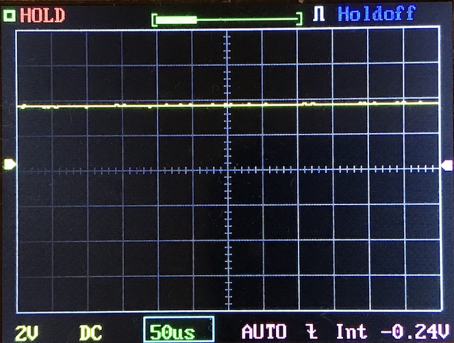 An oscilloscope screen displays a mostly flat yellow waveform near zero on a grid. The settings at the bottom indicate 2V per division and 50 microseconds per division. The screen shows HOLD and Holdoff modes.