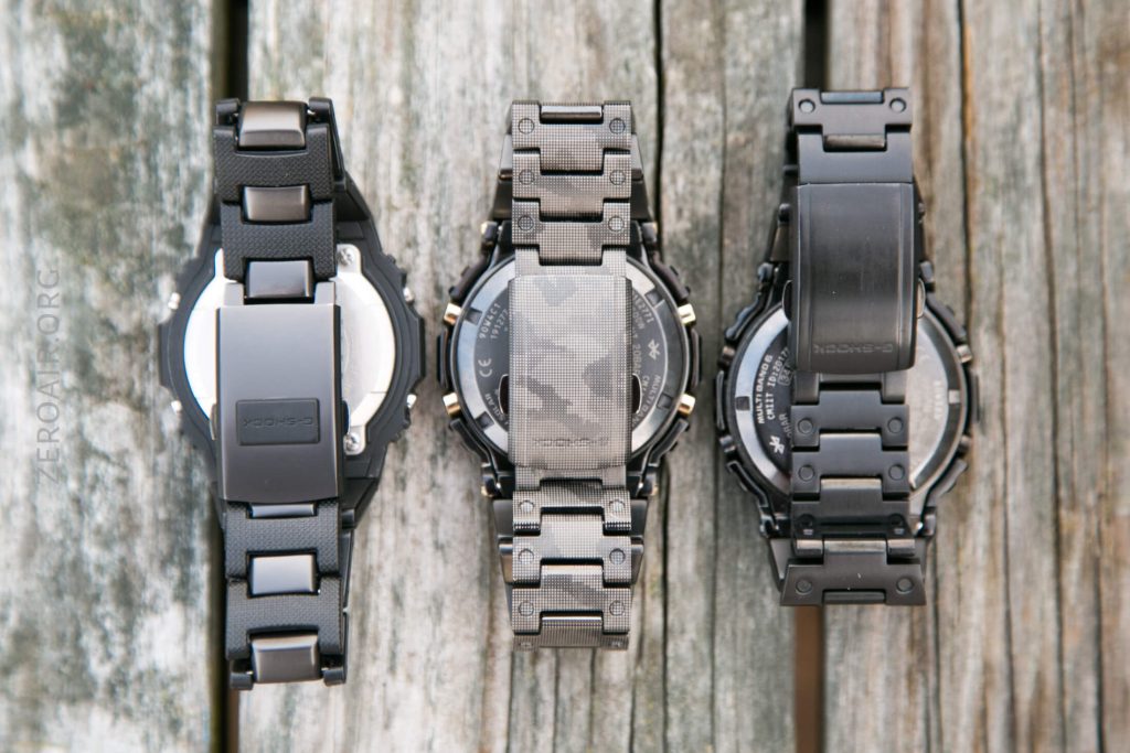Three wristwatches are shown face down on a weathered wooden surface. Each has a different metal or rubber strap design, with the watch case backs and clasps visible.