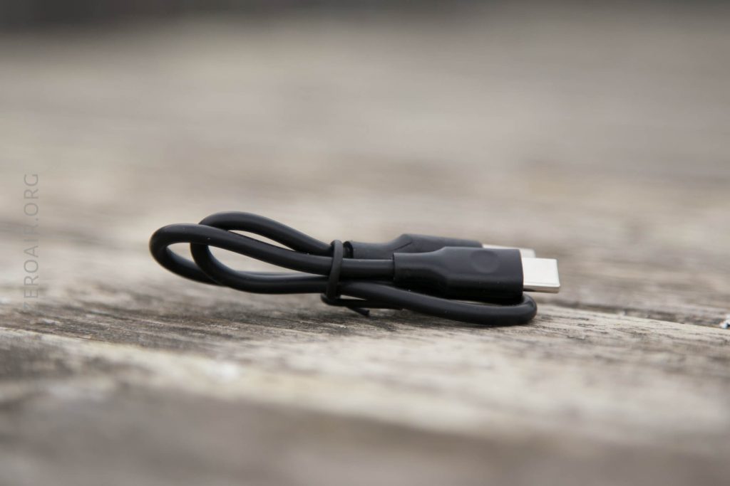 A black USB-C charging cable is coiled and secured with a twist tie, resting on a wooden surface.