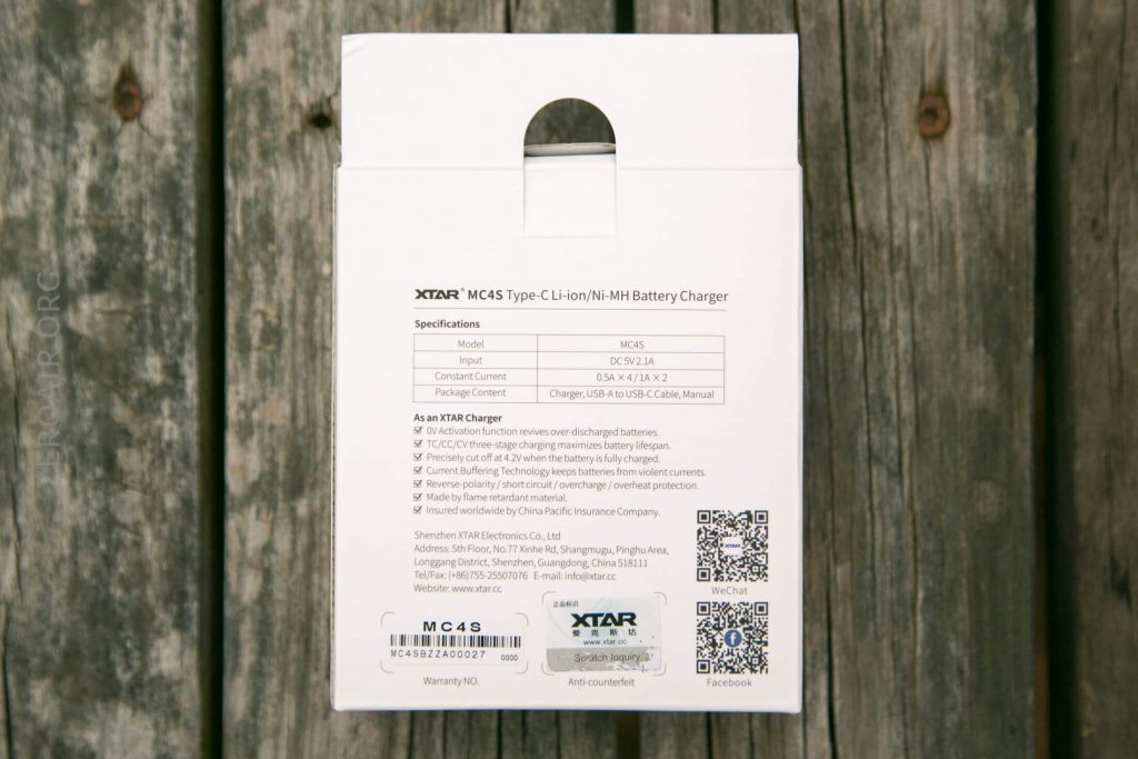 Back of an XTAR MC4S battery charger box showing product specifications, features, QR codes, manufacturer details, and a barcode; the box is placed on a wooden surface.
