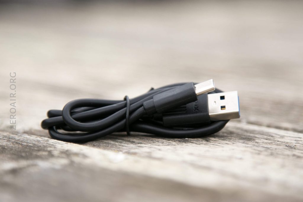 A black USB cable is coiled and resting on a wooden surface. One end has a standard USB-A connector, while the other end has a smaller connector.