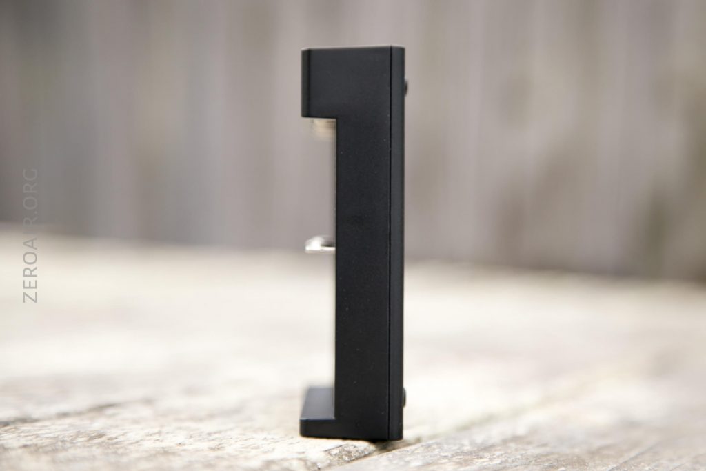 A black, block-shaped object shaped like the number 1 stands upright on a light wood surface with a blurred background.
