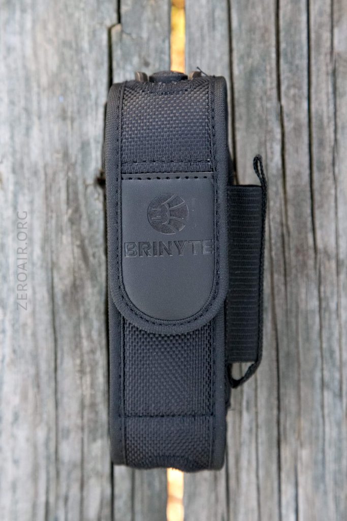 A black nylon case with a flap labeled BRINYTE sits vertically against weathered wooden boards. The stitching and texture of the case are visible.