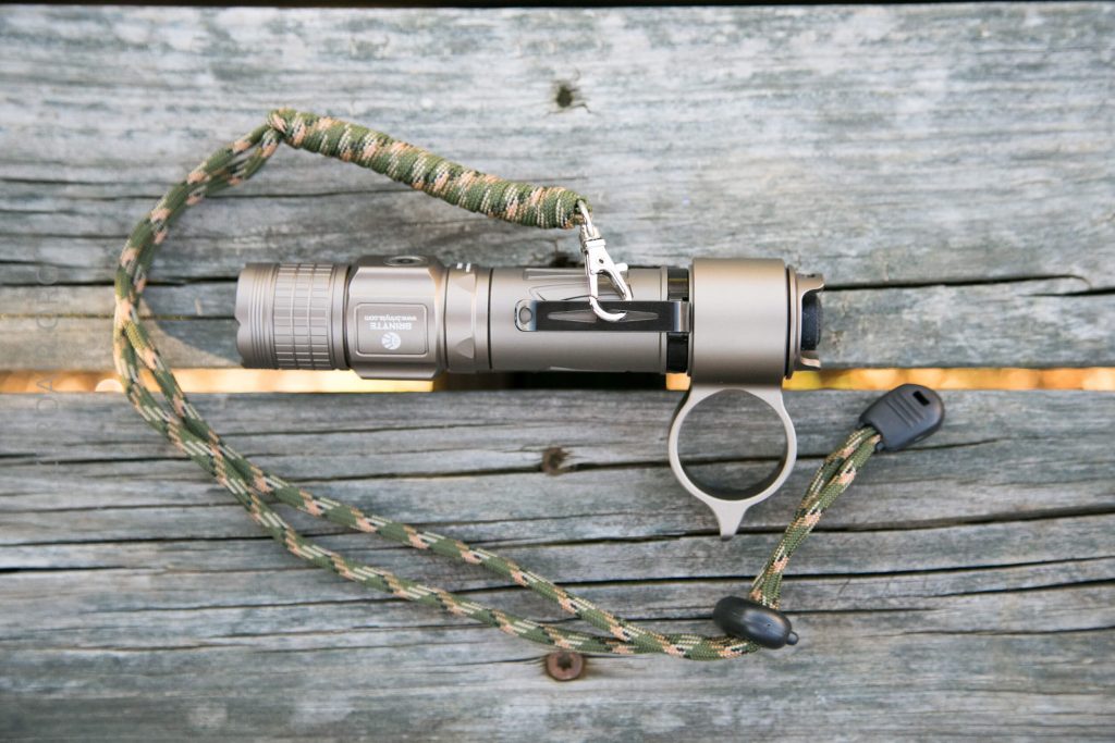 A compact flashlight with a camouflage-patterned wrist strap and a metal ring is placed on a weathered wooden surface.