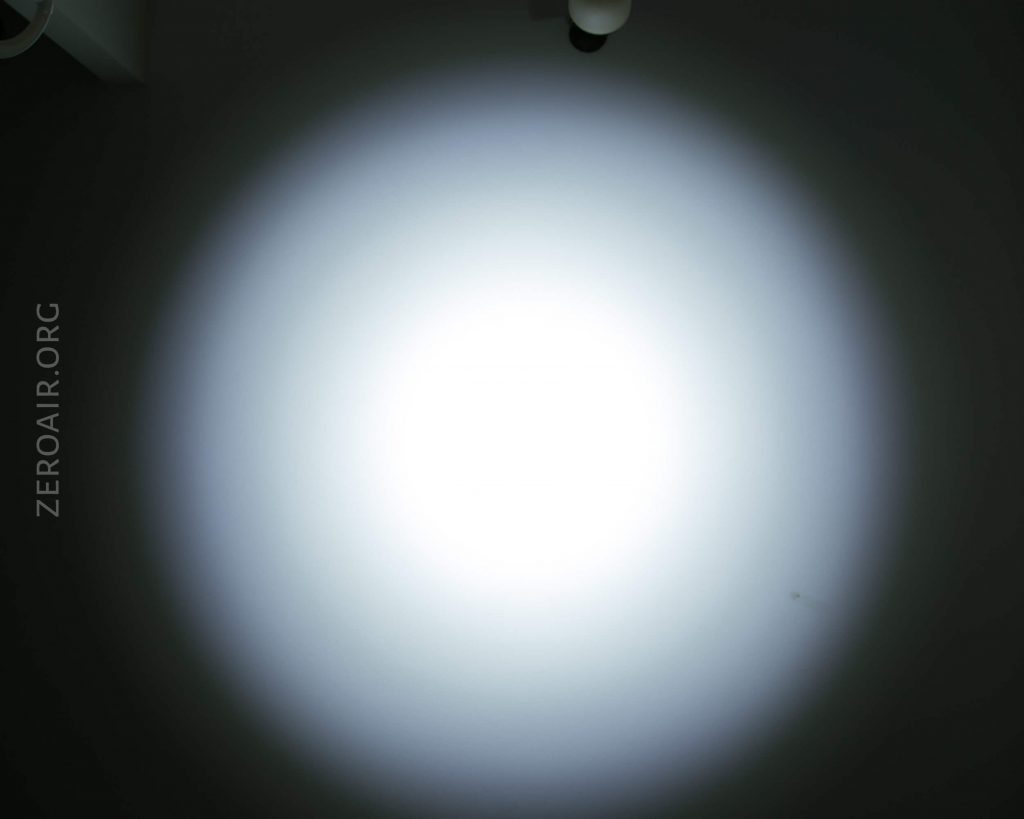 A bright, circular beam of white light is projected onto a dark surface. The light fades gradually towards the edges. The text ZEROAIR.ORG is vertically visible on the left side of the image.