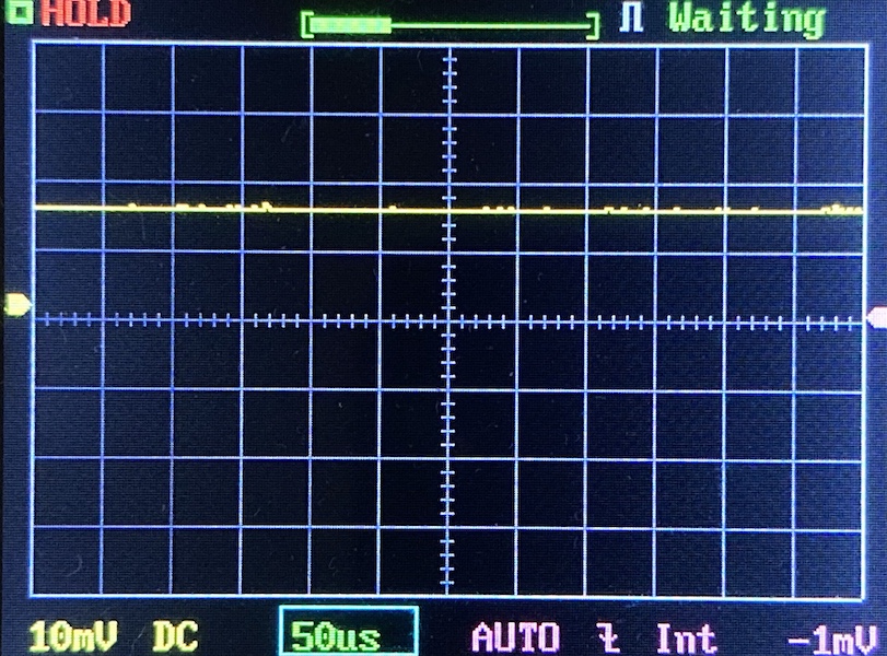 Oscilloscope screen showing a mostly flat yellow waveform near the zero line, with settings including 10mV per division, 50 microseconds per division, and a vertical offset of -1mV. The status reads “HOLD” and “Waiting.”